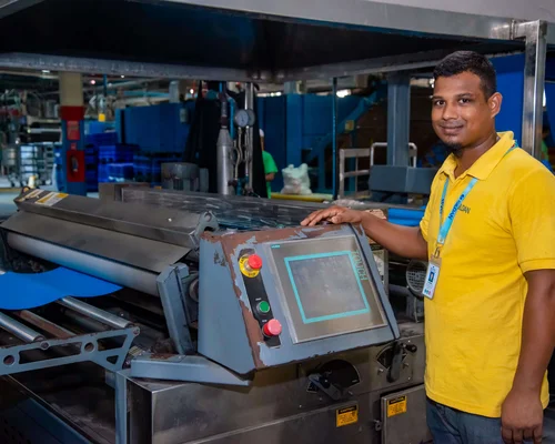 Un hombre vestido de amarillo está de pie junto a una máquina y sonríe.
