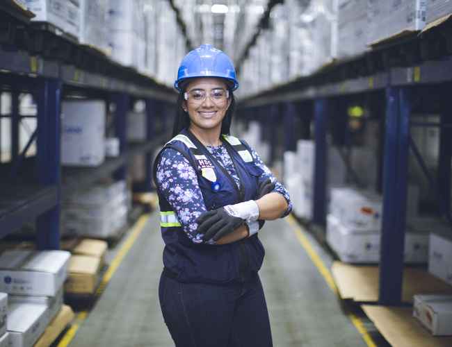 Une femme portant un gilet de sécurité et un casque sourit à la caméra.