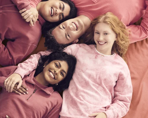 Two women and two men are lying down wearing pink Comfort Colors sweaters smiling.