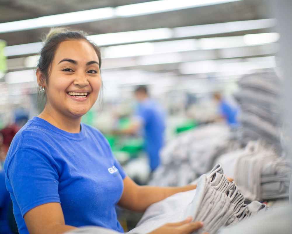 A man standing in the yarn spinning facility next to yarn cones smiling at the camera