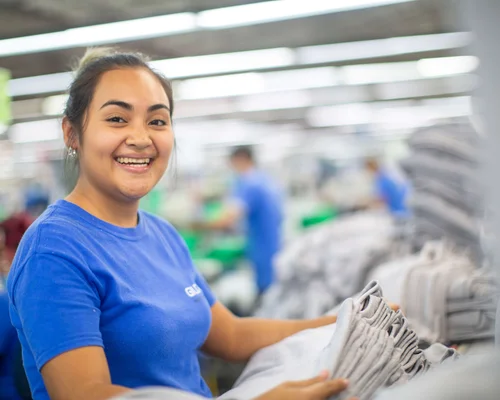 A woman holding a pile of grey folded Gildan shirts.