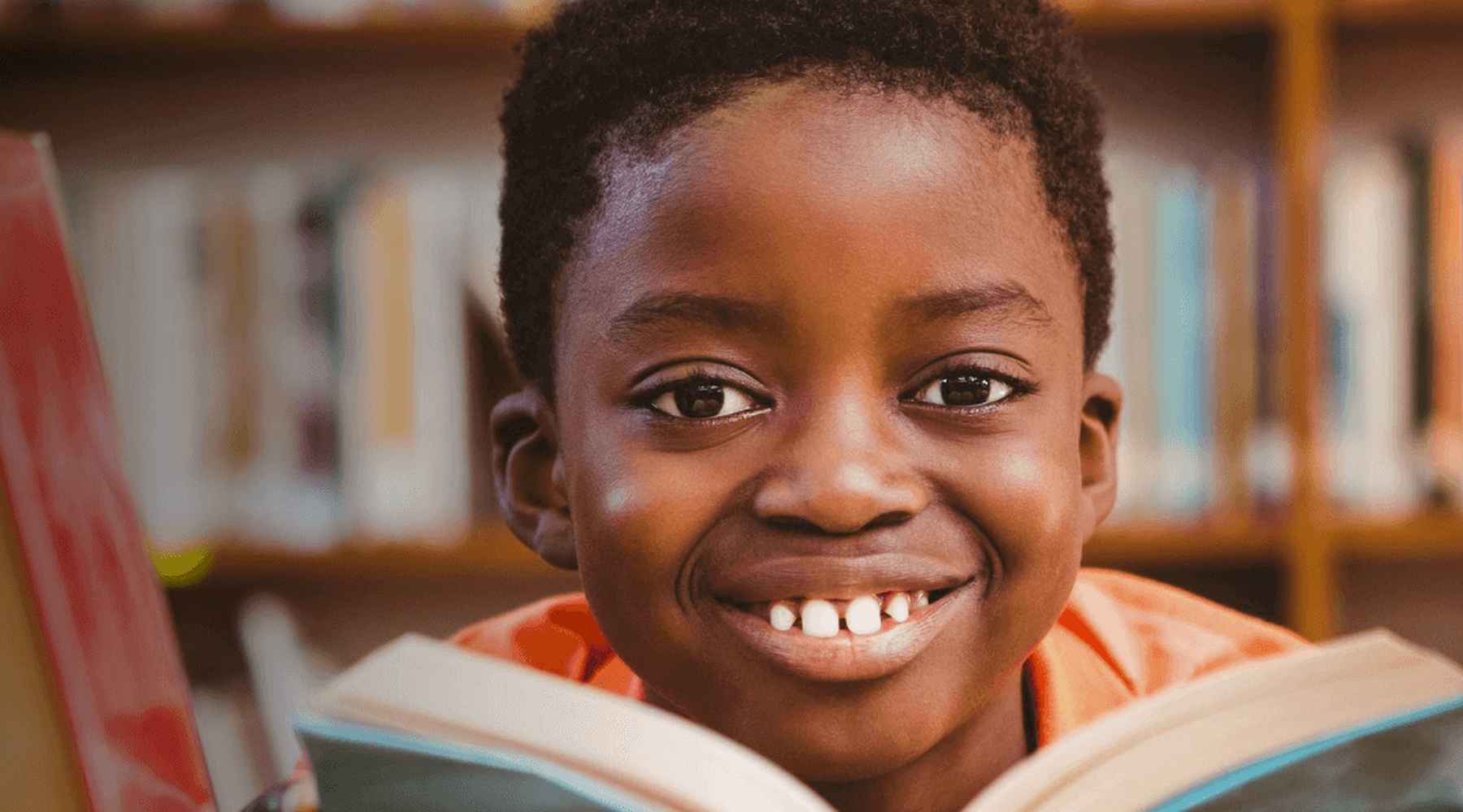 Un enfant tient un livre et sourit à la caméra.