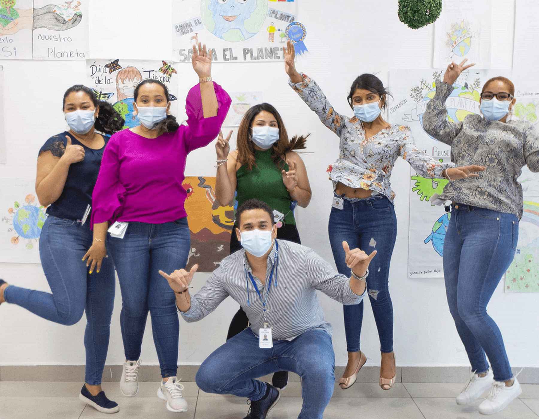 Six Gildan employees in Honduras are jumping. There are Earth Day drawings posted in the background.