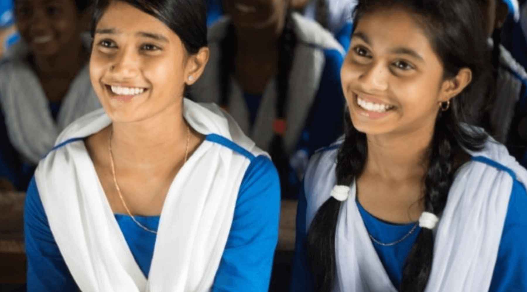 Two girls from Bangladesh’s Room to Read program are smiling and wearing the same blue dress.