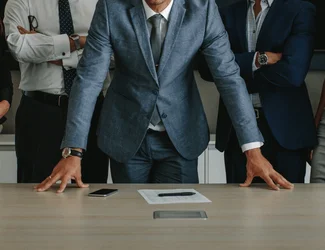 Tres hombres miran a la cámara con los brazos cruzados y apoyados en la mesa de una oficina.