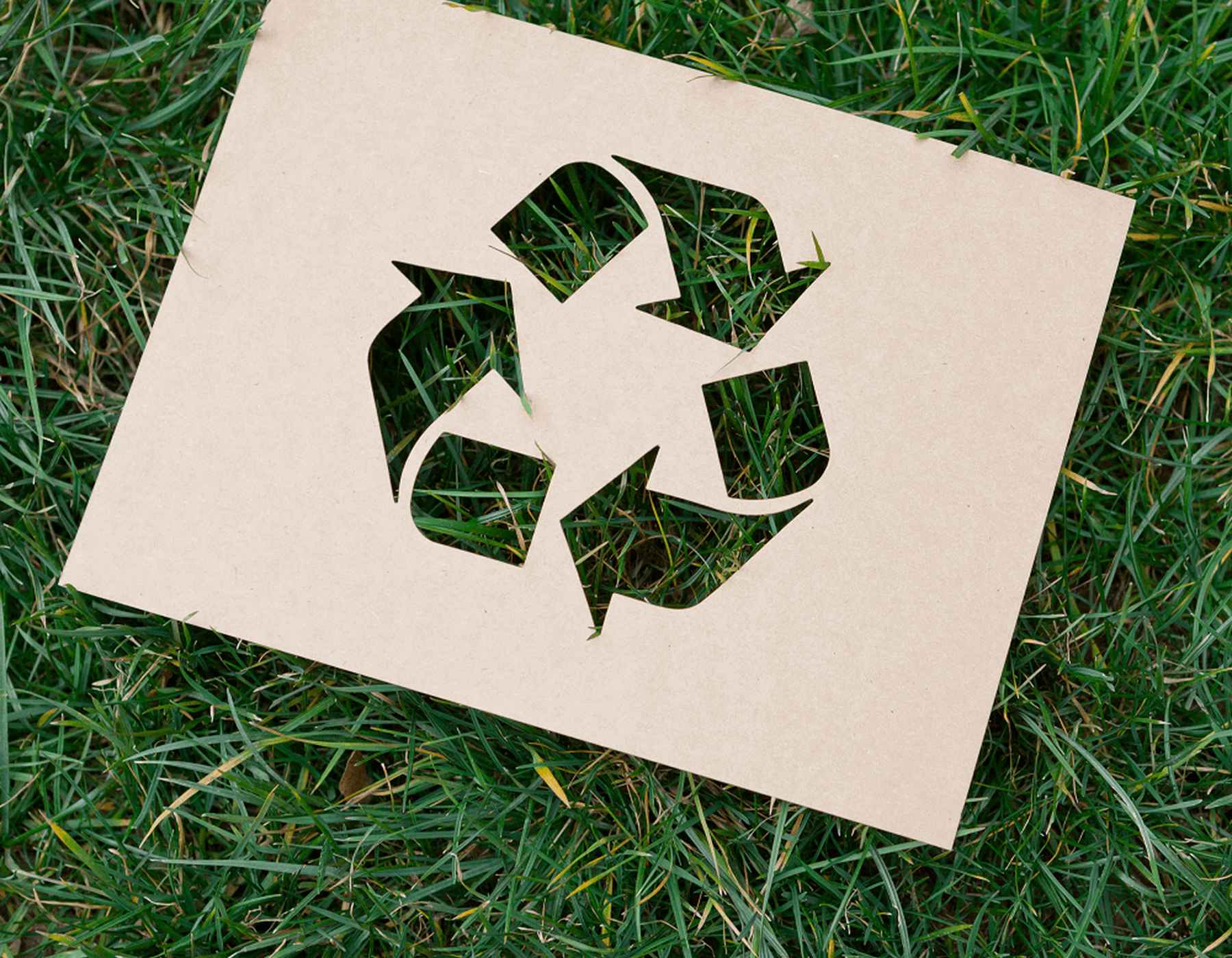 Un papel con una forma recortada del símbolo de reciclaje yace sobre la hierba.