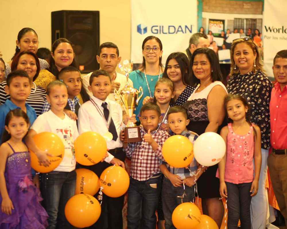 Un grupo de niños y empleados de Gildan en Honduras sonríen juntos mientras sostienen un trofeo.