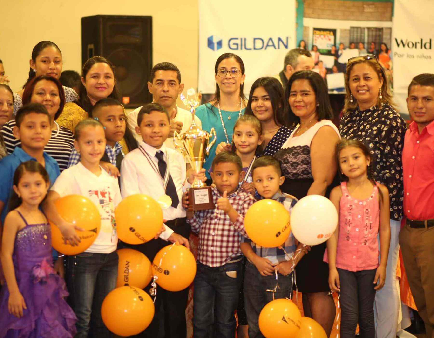 A group of children and Gildan employees in Honduras are smiling together while holding a trophy.