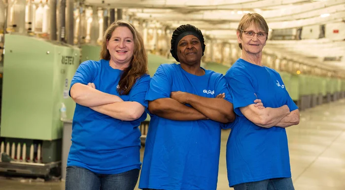 Tres empleados de Gildan se cruzan de brazos y sonríen en las instalaciones de hilado.