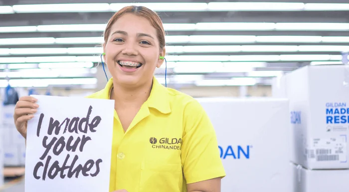 Mariela is smiling and holding a sign that reads “I made your clothes”.