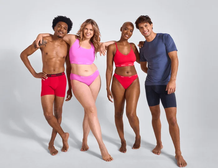 Four adults standing side by side against a neutral gray background wearing muti-colored innerwear.