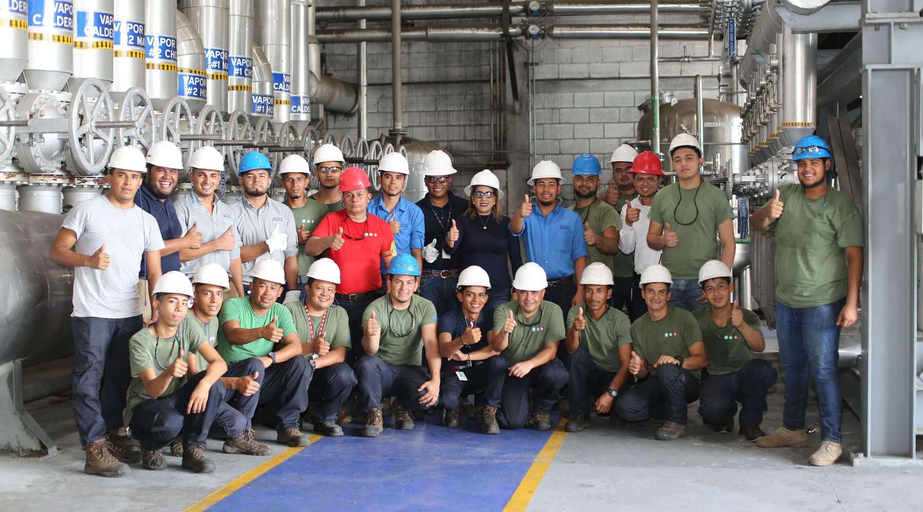 A group of Gildan employees wearing hard hats smiling and holding a thumbs up the camera.