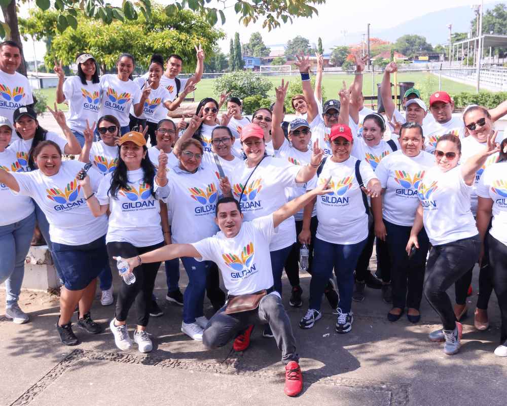 Gildan employees are outside wearing white Gildan t-shirts and smiling at the camera.