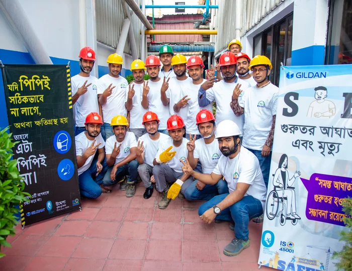 Un grupo de empleados con cascos de seguridad sonríen a la cámara sosteniendo signos de paz.