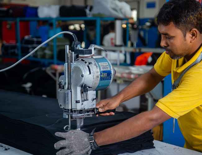 Au Bangladesh, un homme vêtu d'une chemise jaune utilise une machine à découper le tissu.