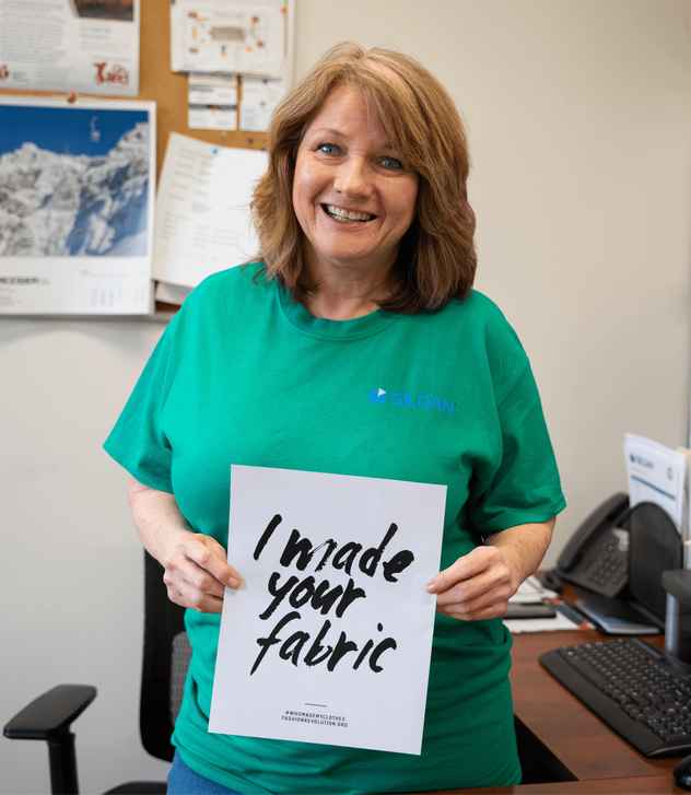 Lisa is smiling at the camera and holding a sign that reads “I made your fabric”.