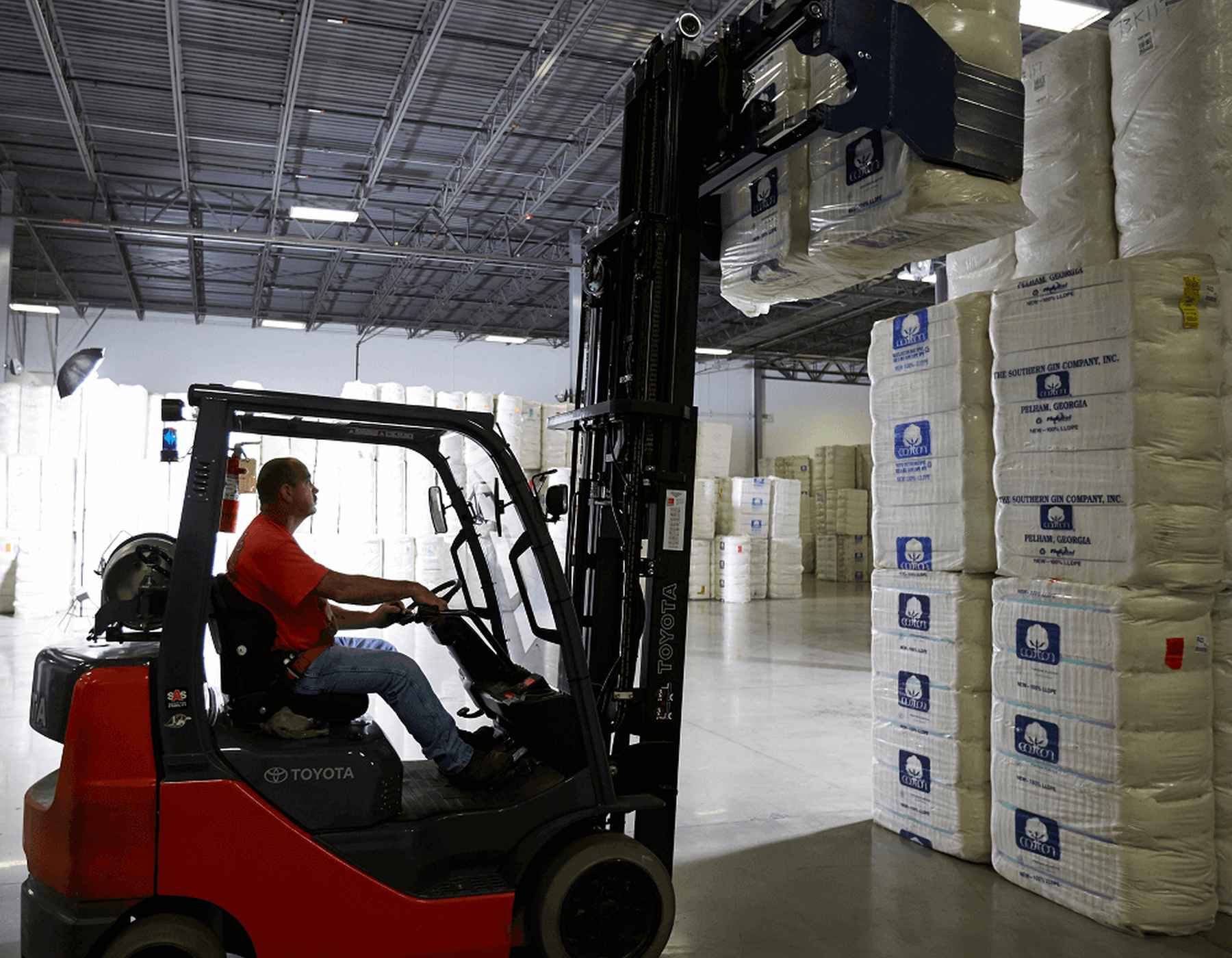 A Gildan employee is using a forklift to lift a package of cotton.