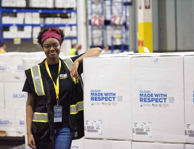 A female employee is standing next to a pile of boxes with the Made With Respect logo.