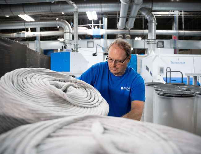 A male employee is moving a bin of yarn fibre in the Eden yarn spinning facility.