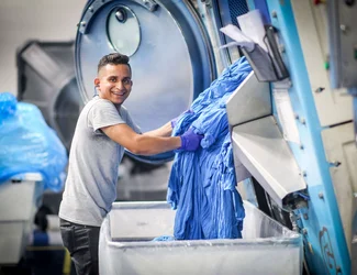 A man in Honduras is taking out wet blue fabric from a machine.