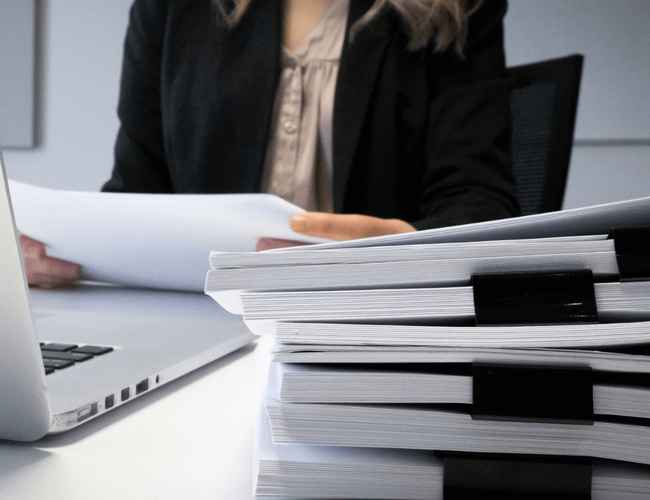 A woman is looking through a pile of papers at the office