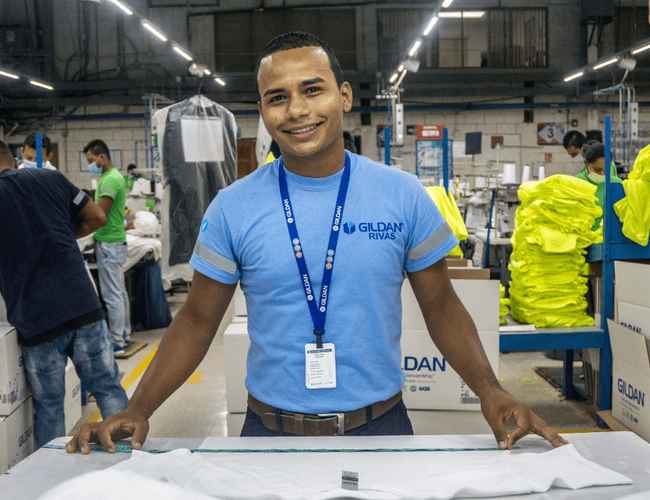 Un empleado de Gildan lleva un cordón de Gildan y una camisa azul.