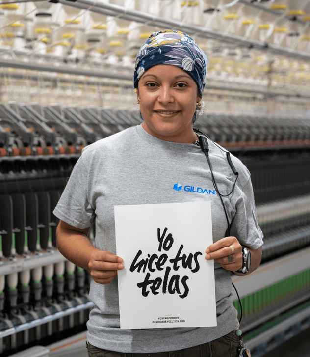 Pureza is smiling and holding a sign that reads “I made your fabric”.