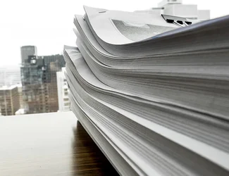 A stack of paper is piled on top of a desk.