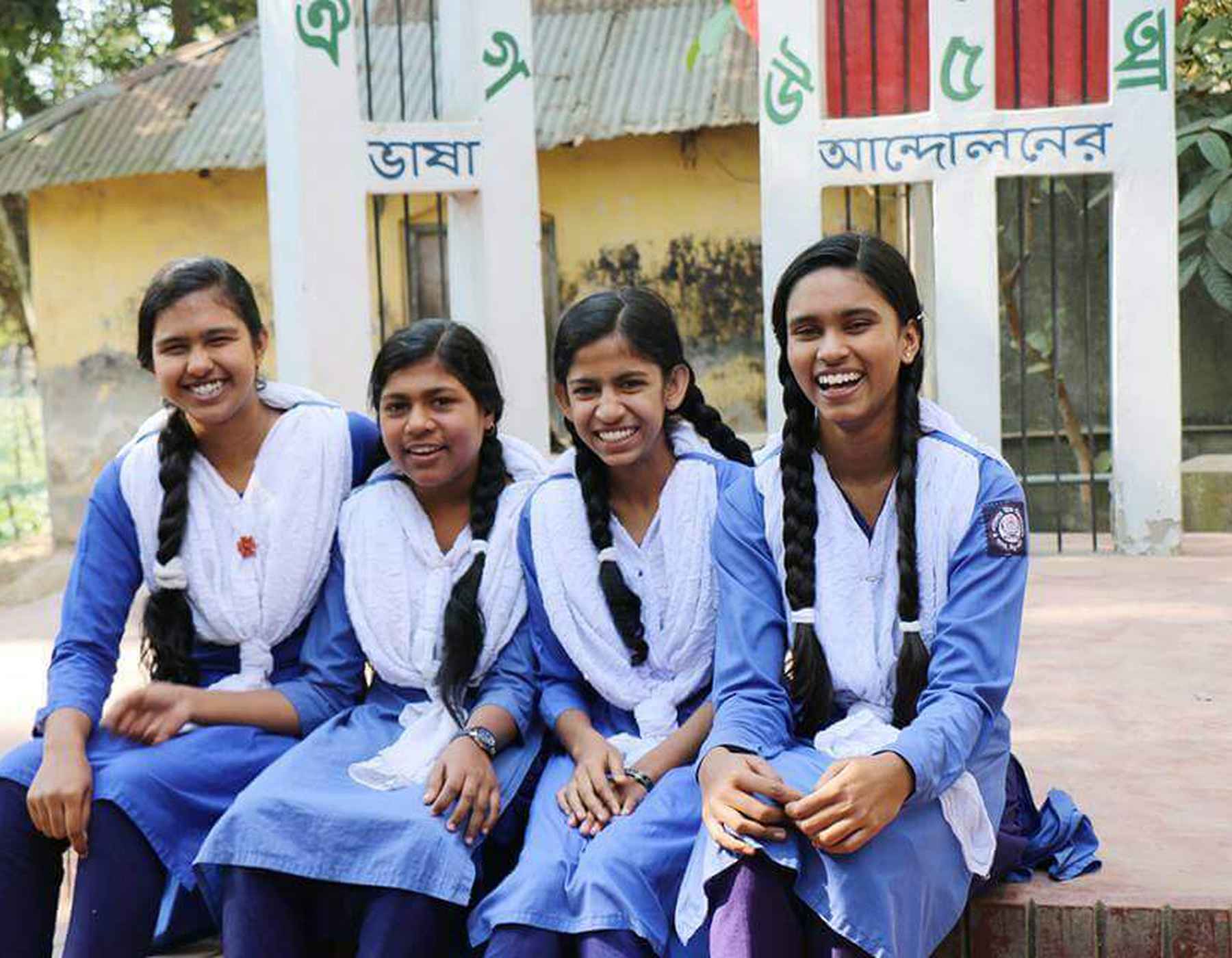 Quatre jeunes femmes au Bangladesh rient en portant un uniforme bleu et des foulards blancs.