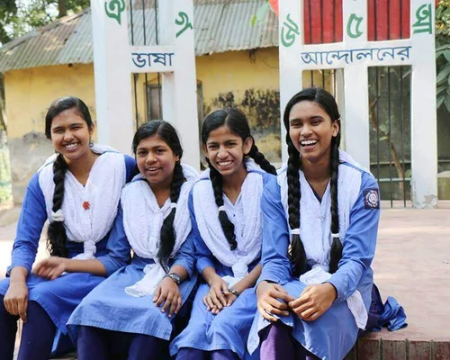 Cuatro mujeres jóvenes en Bangladesh se ríen mientras visten un uniforme azul y bufandas blancas.