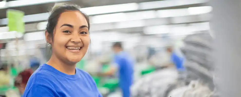 Un homme debout dans l'installation de filage à côté de cônes de fil, souriant à l'appareil photo.