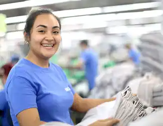 A sewing employee wearing a mask and safety goggles is using a sewing machine.