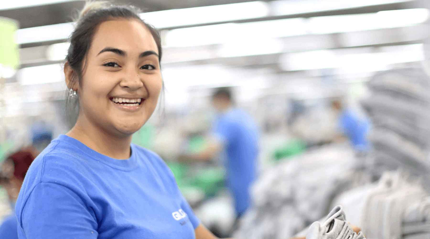 A Gildan sewing employee is smiling at the camera.