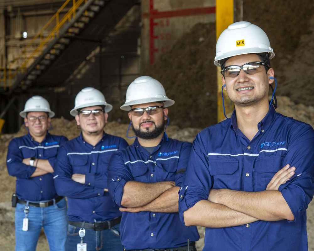 Cuatro empleados masculinos llevan camisetas Gildan y cascos sonriendo a la cámara con la Biomasa.