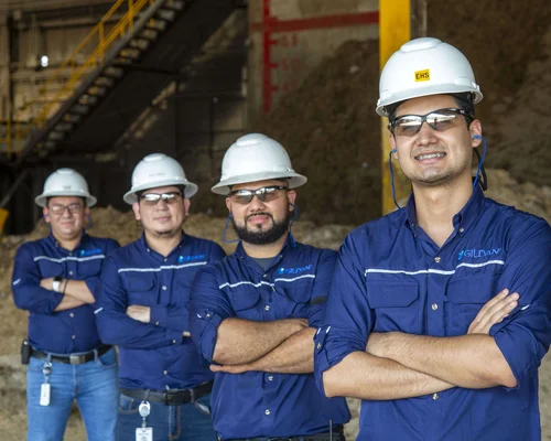 Cuatro empleados masculinos llevan camisetas Gildan y cascos sonriendo a la cámara con la Biomasa.