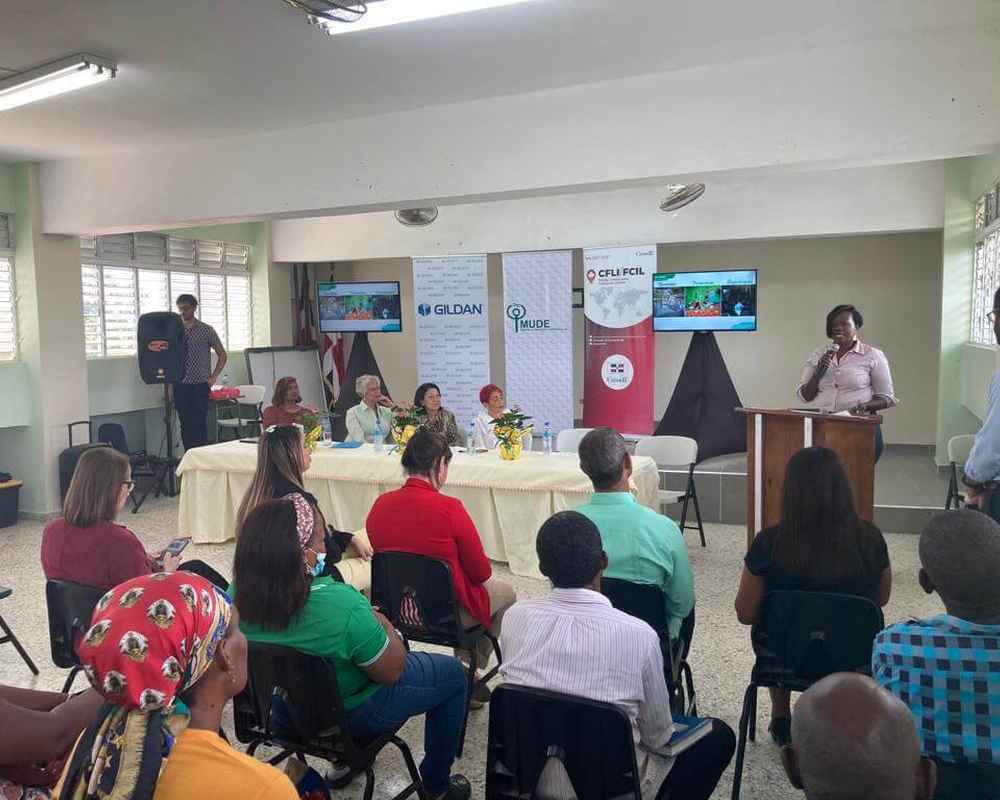 Una mujer habla por un micrófono frente a un grupo de empleados de Gildan.