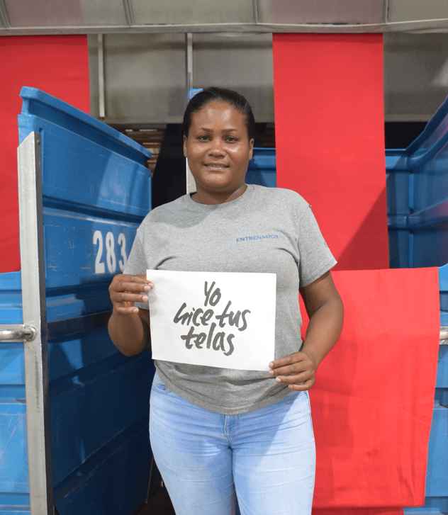 Yafreysy is smiling at the camera and holding a sign that reads “I made your fabric”.
