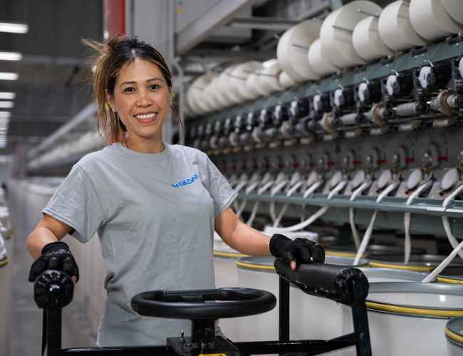 A yarn-spinning employee in the U.S. is standing in front of yarn spinning machine and smiling.