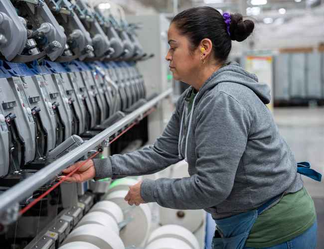 A woman in a grey hoodie is using the yarn spinning machines in the United States.