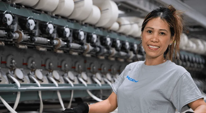 Una mujer sonríe junto a las máquinas de hilar.