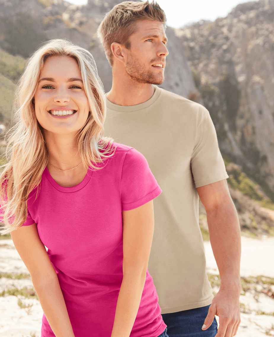 Una mujer y un hombre con camisetas de Gildan™ en la playa sonriendo a la cámara.