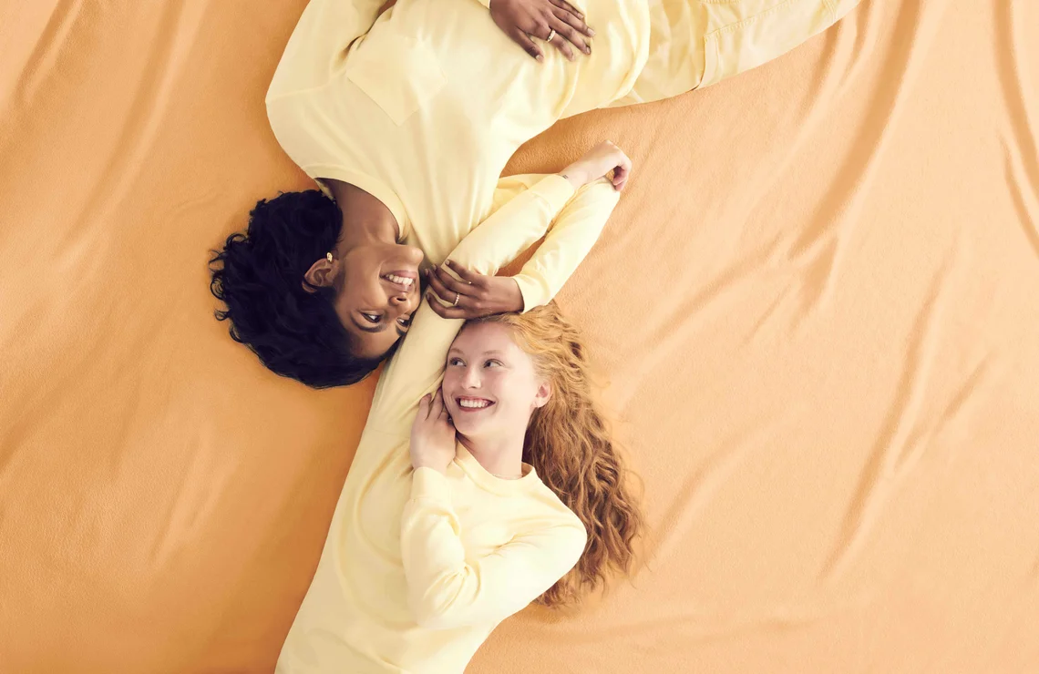 Two models wearing yellow Comfort Colors clothing, lying against a yellow backdrop